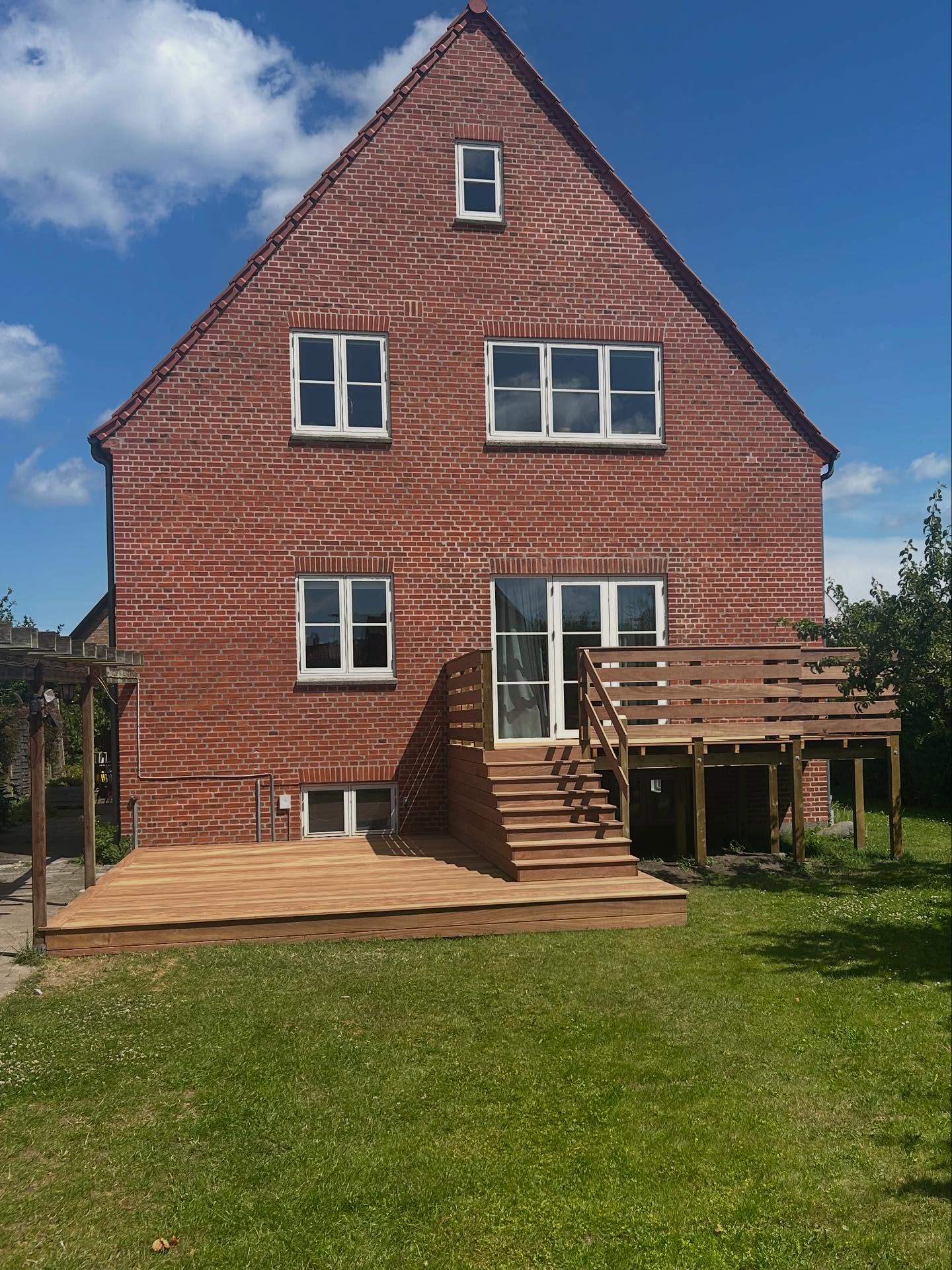 Træterrasse med flere niveauer og integreret trappe foran et murstenshus